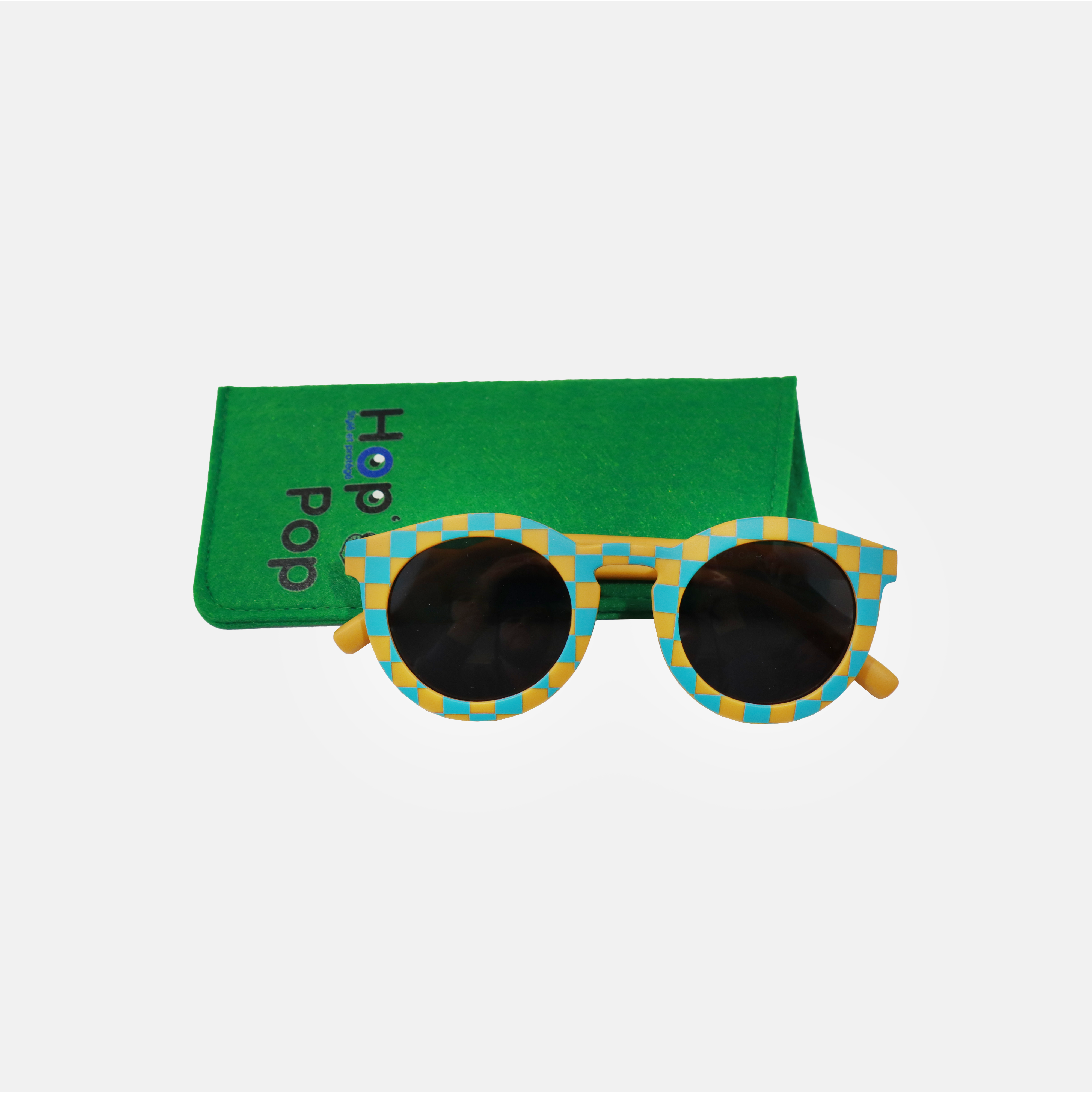 Lunette de soleil pour adulte à monture ronde motif vichy bleu et moutarde, posée devant leur étui de rangement en feutrine verte marqué "Hop'Pop".